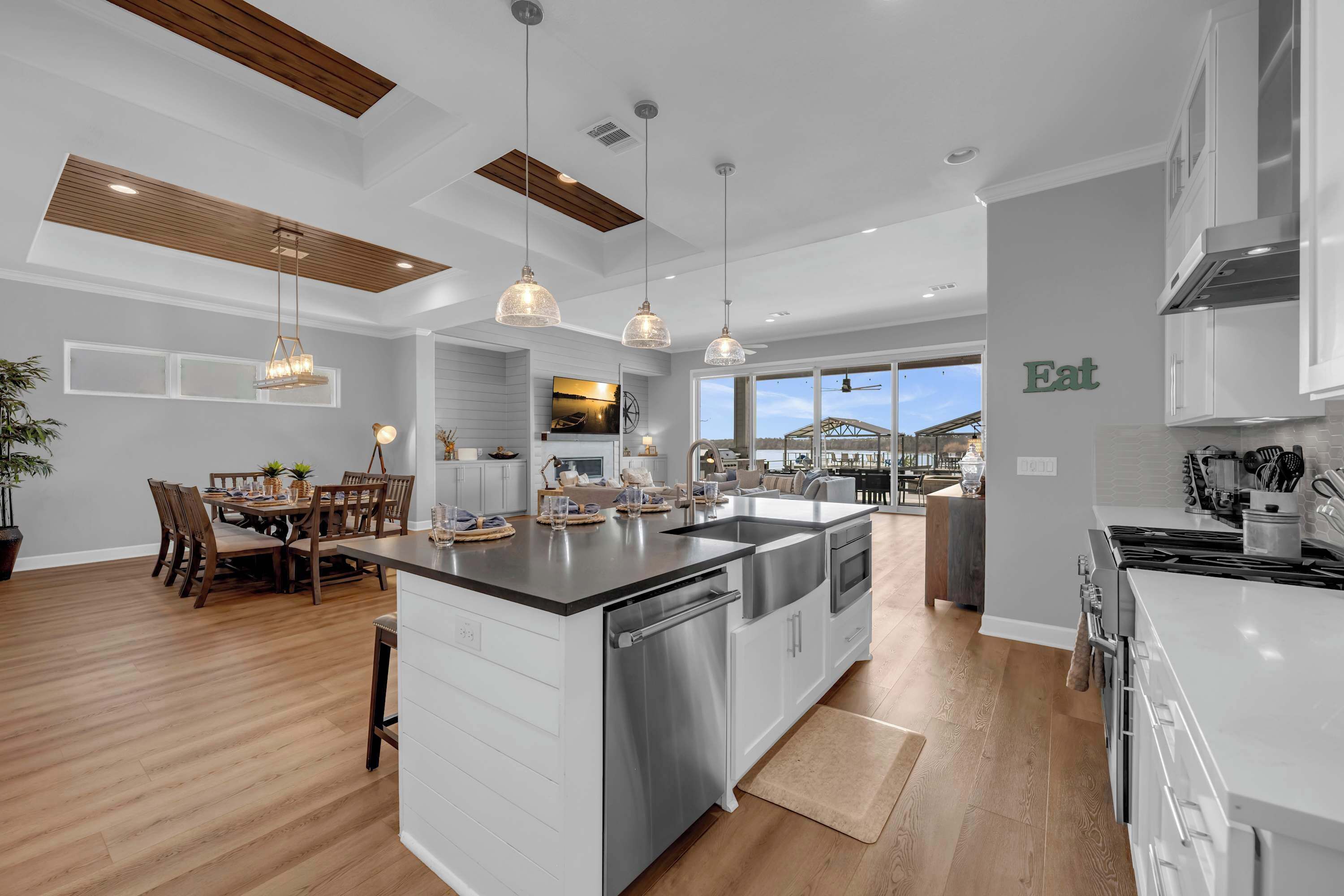 Une cuisine moderne dotée d’un îlot central, de luminaires suspendus et d’un coin repas avec une table et des chaises en bois.