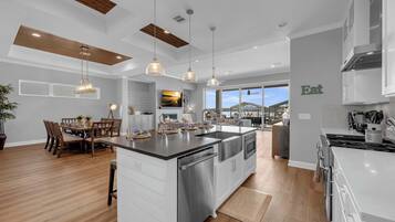 Une cuisine moderne dotée d’un îlot central, de luminaires suspendus et d’un coin repas avec une table et des chaises en bois.