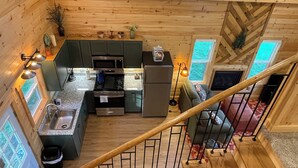A wooden cabin interior with a kitchen, dining area, and a staircase.