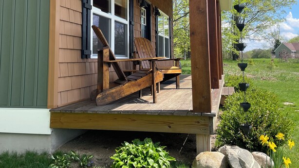 A wooden house with a porch, a bench, and a garden with flowers and rocks.