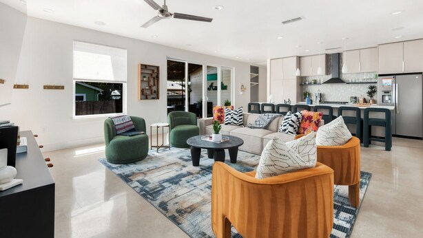 A modern living room with a sofa, armchairs, and a coffee table. There is a kitchen area with cabinets and a refrigerator.