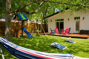 Ein Garten mit Schaukel, Rutsche und Poolbereich mit Liegestühlen.