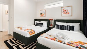 A hotel room with two beds, white bedding, a black and white patterned rug, and artwork on the walls.