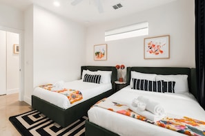 Una habitación de hotel con dos camas, ropa de cama blanca, un tapete blanco y negro estampado y obras de arte en las paredes.