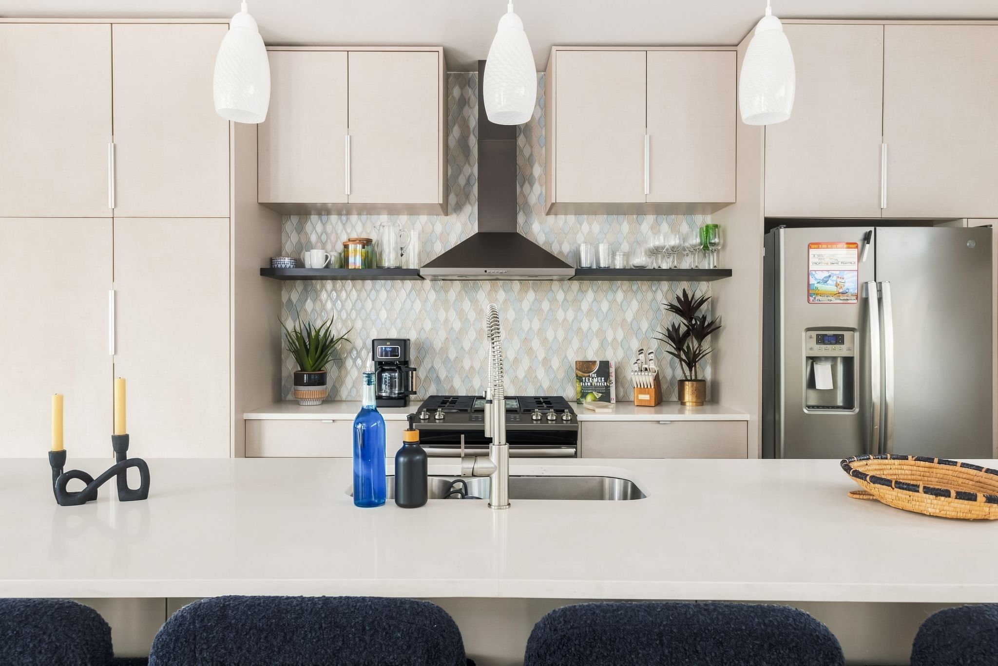 Cozinha moderna com ilha central, eletrodomésticos de aço inoxidável e iluminação pendente.