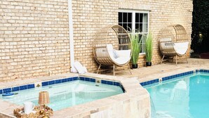 Una piscina con un muro de ladrillo y dos sillas de mimbre.