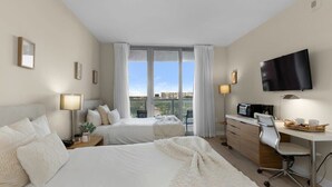 Hotellihuone, jossa on kaksi sänkyä, työpöytä, televisio ja parveke, jolta on näkymä.