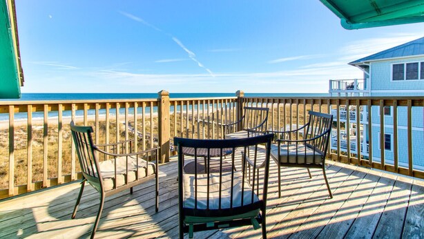 Terraza de madera con una mesa y sillas que da a una playa.