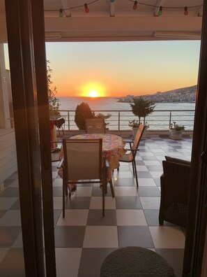 Ein Balkon mit kariertem Boden, einem Tisch mit blumigem Tischläufer, Stühlen und Topfpflanzen.
