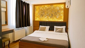 Habitación de hotel con una cama grande, cabecera de madera, mesita de noche, espejo y ventana con cortinas.