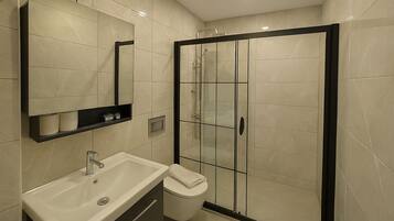 A modern bathroom with a large mirror, a sink, a toilet, and a glass-enclosed shower area.