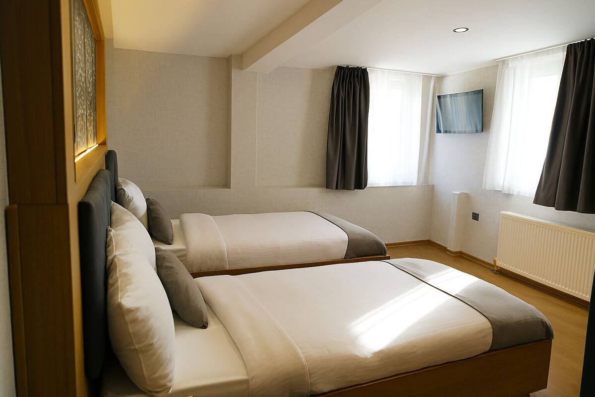 A hotel room with two beds, a TV mounted on the wall, and a window with curtains.