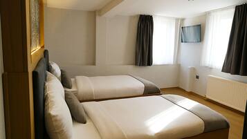 Une chambre d’hôtel avec deux lits, un téléviseur fixé au mur et une fenêtre avec des rideaux.