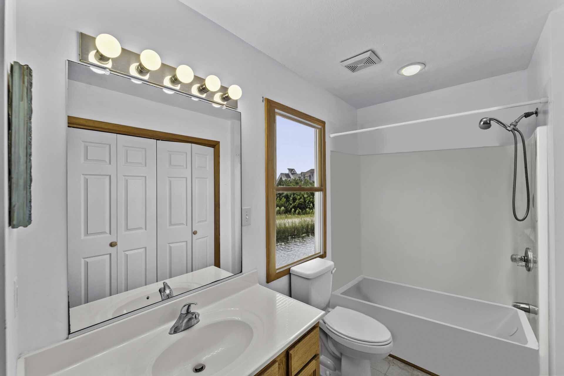 Un baño moderno con un espejo grande, tocador, inodoro y bañera.
