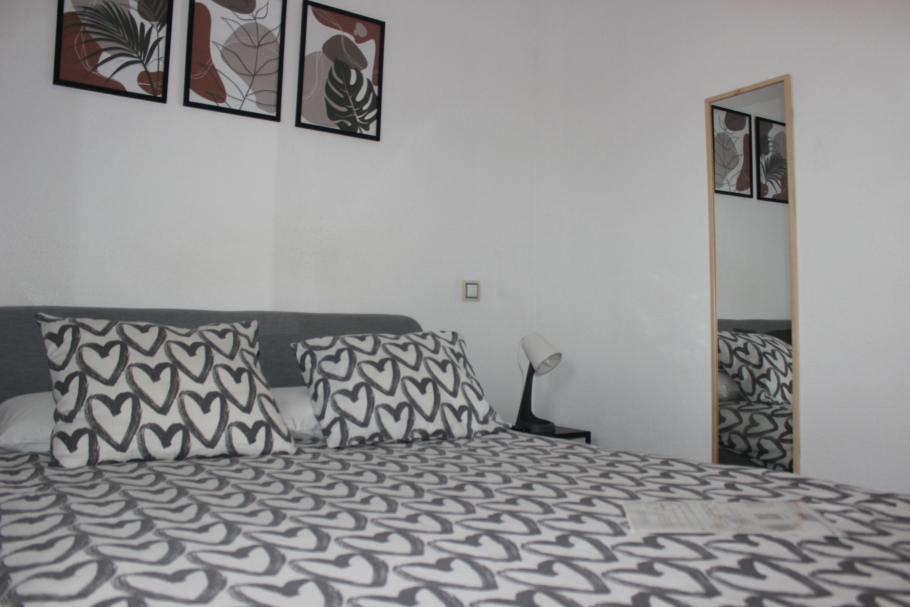 Un dormitorio con una cama, almohadas estampadas con motivos de corazón, una lámpara de noche y arte abstracto en la pared.