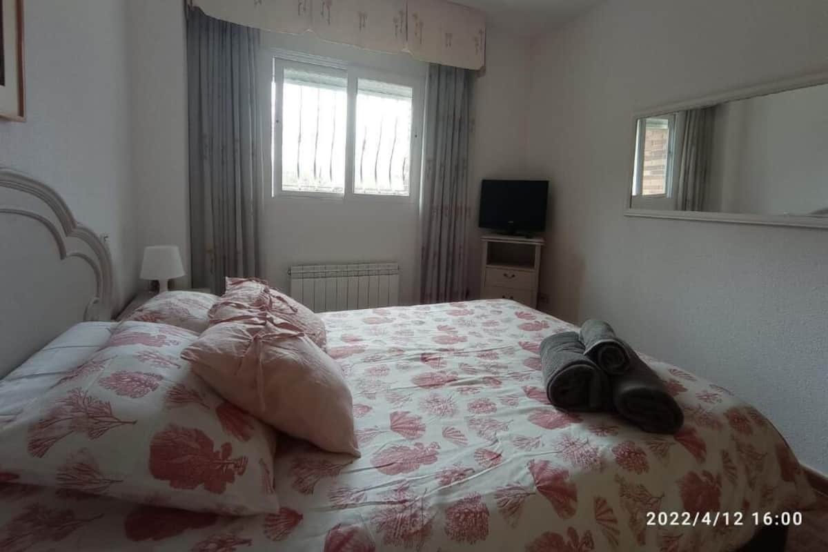 A bedroom with a bed, a television, a radiator, and a window with curtains.