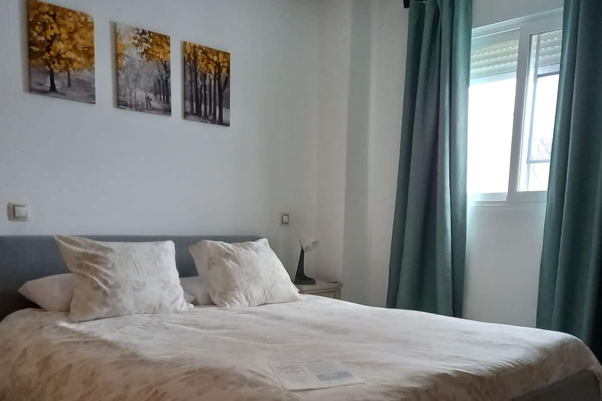 A bedroom with a bed, two pillows, a nightstand, and three wall paintings.