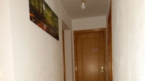 A narrow hallway with a wooden door at the end, a light fixture above, and a painting on the wall. - Casa de Huéspedes Villa de las Hortensias (Bustarviejo)