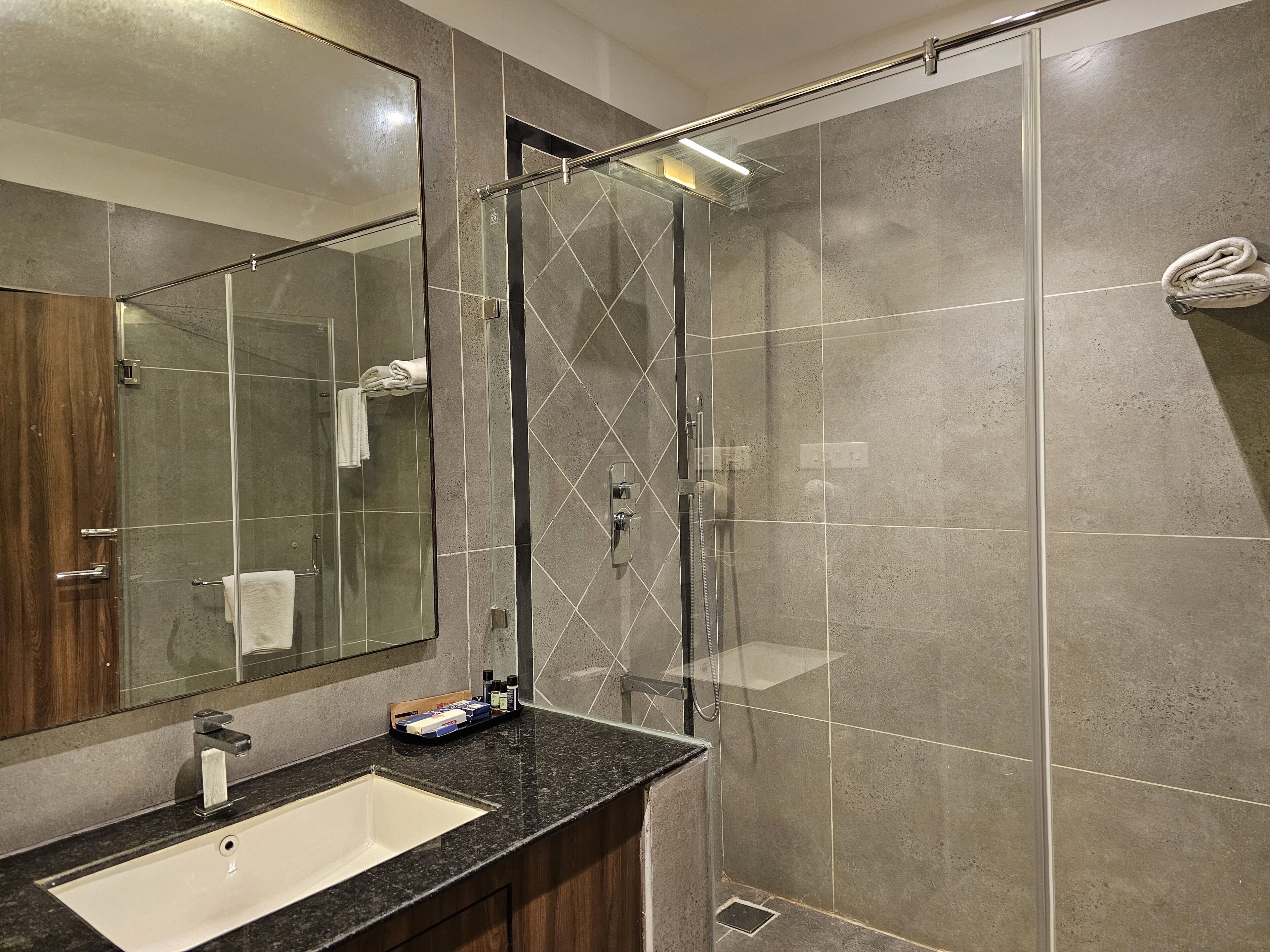 A modern bathroom with a glass-enclosed shower, a large mirror, and a granite countertop.