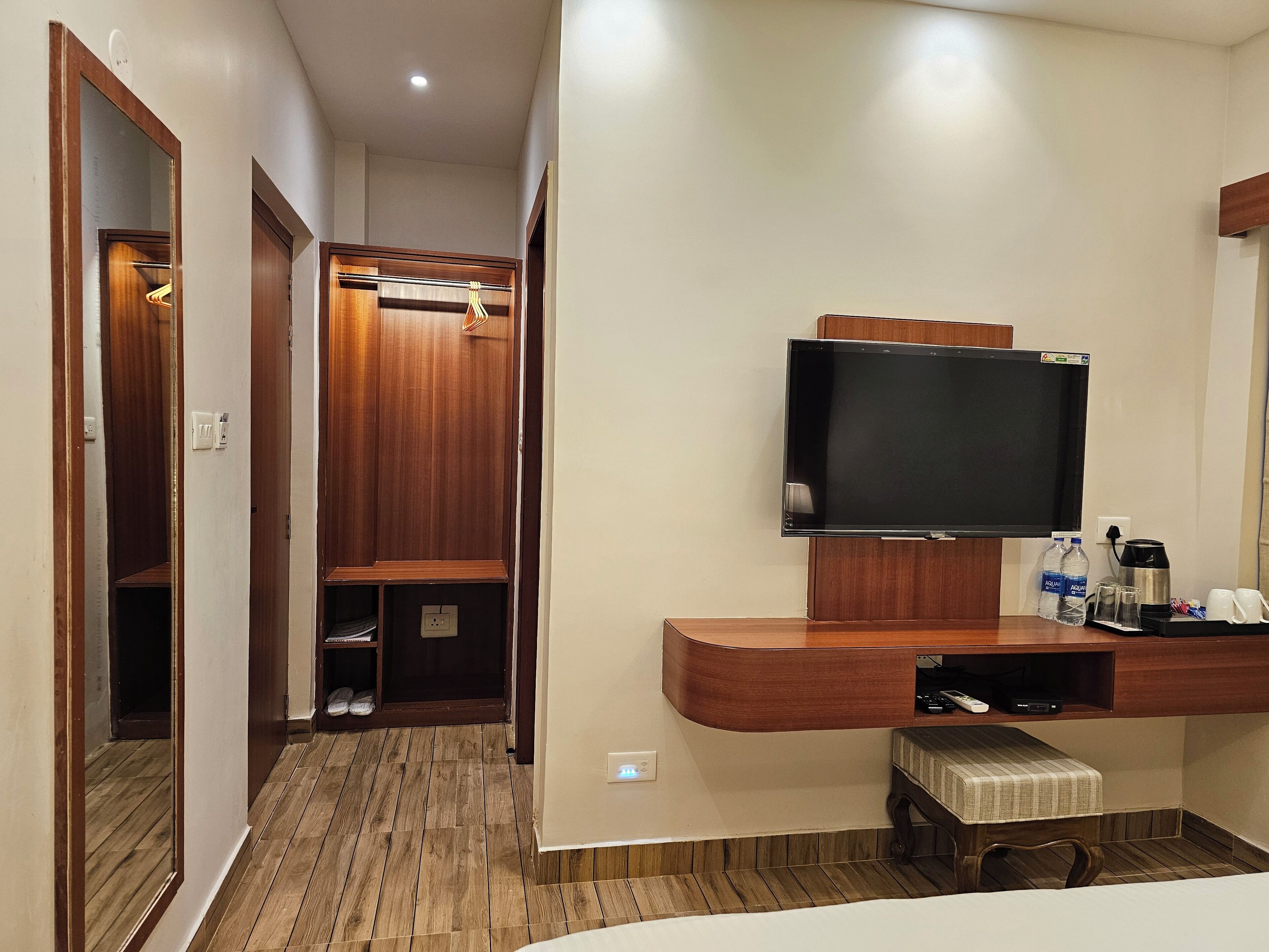 Habitación de hotel con un armario de madera, un televisor montado en un mueble de madera, una mesita con una bandeja y un banco.