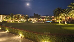 A nighttime view of a resort with a pool, palm trees, and a building with illuminated windows. - The creek boutique resort & spa (Bolpur)