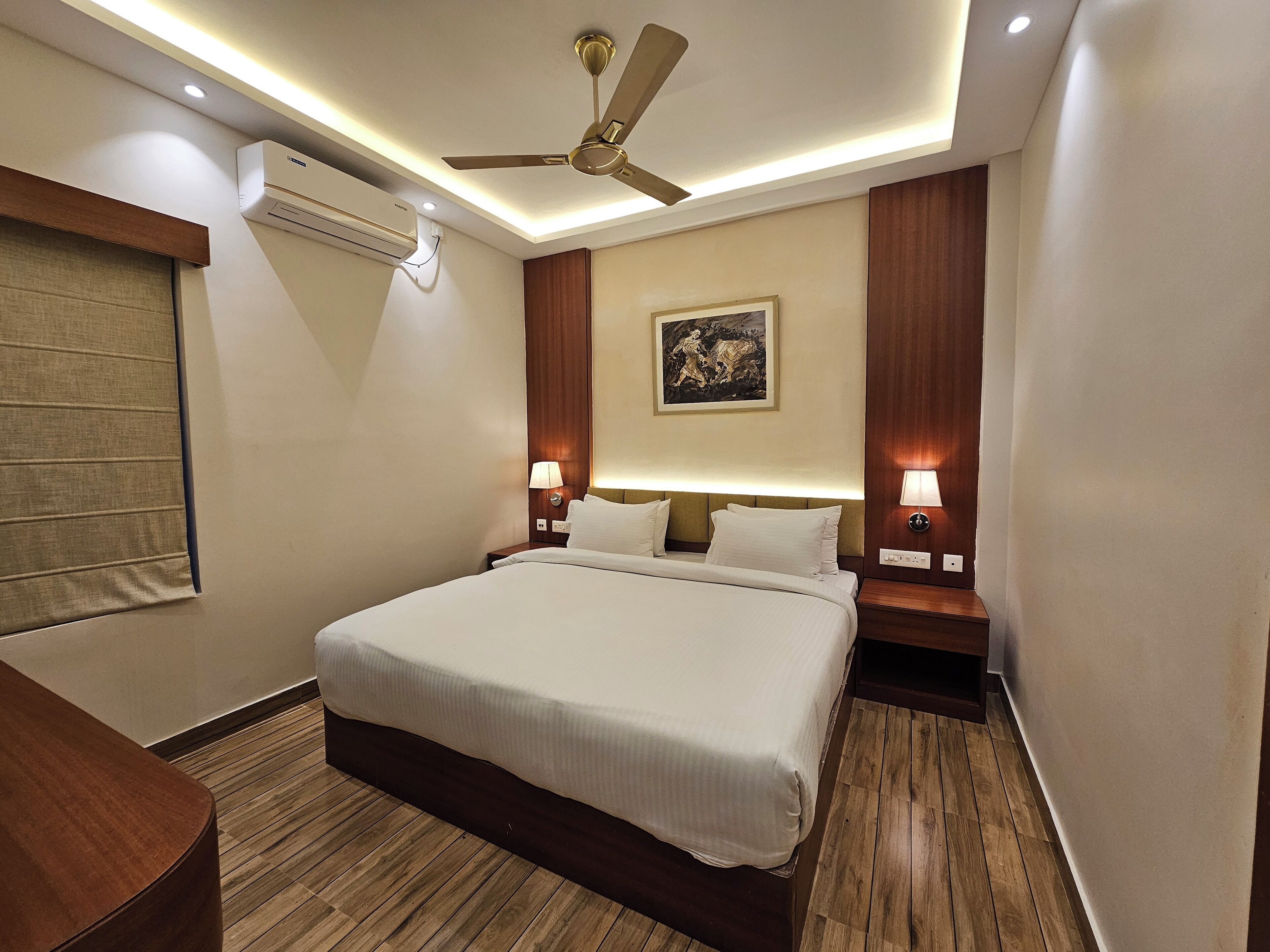 Une chambre d’hôtel avec un grand lit, un ventilateur de plafond, un climatiseur mural, des lampes de chevet et un tableau au mur.