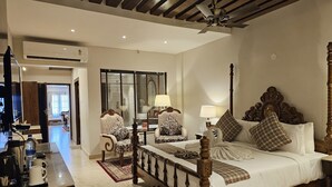 A spacious hotel room with a large bed, two chairs, a desk with a coffee maker, and a television. - The creek boutique resort & spa (Bolpur)