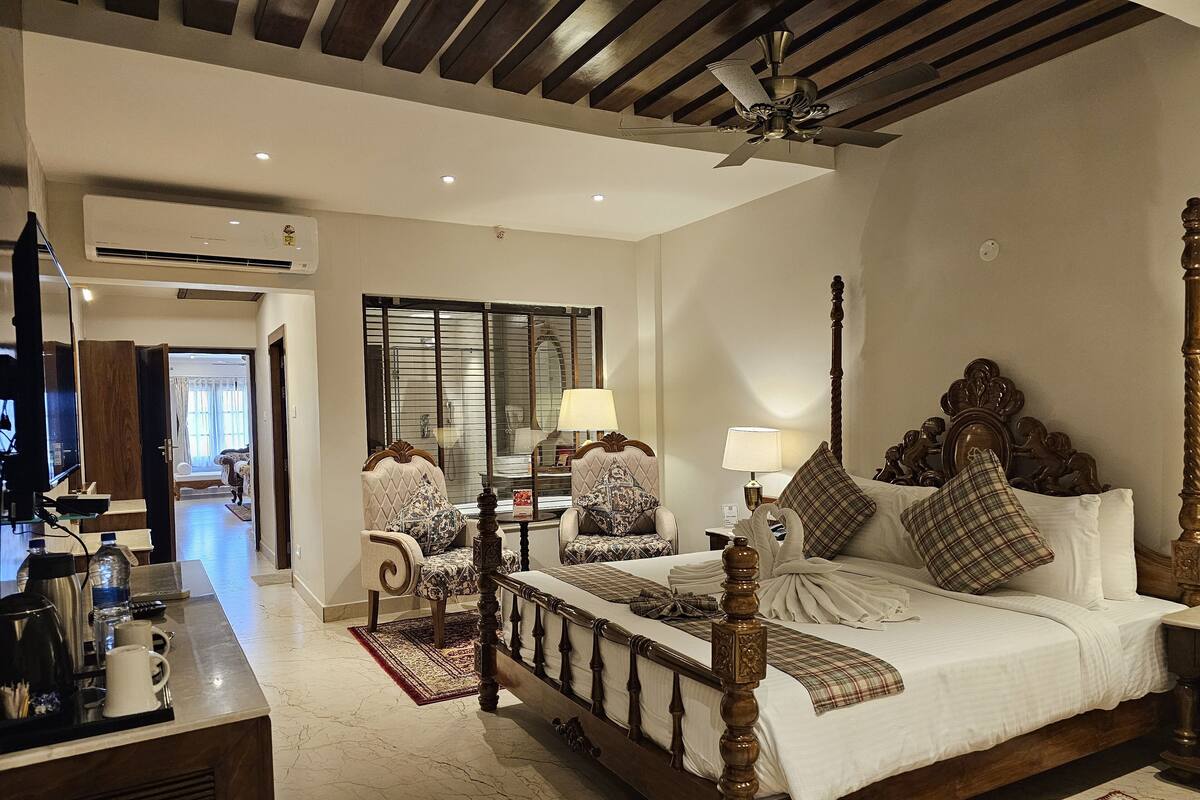 A spacious hotel room with a large bed, two chairs, a desk with a coffee maker, and a television.
