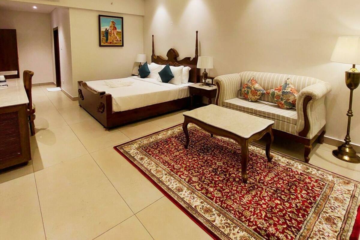 A hotel room with a bed, a sofa, a coffee table, a ceiling fan, and a painting on the wall.
