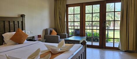 Une chambre d’hôtel avec un lit, une chaise, une table et une vue sur un jardin, visible à travers de grandes fenêtres.