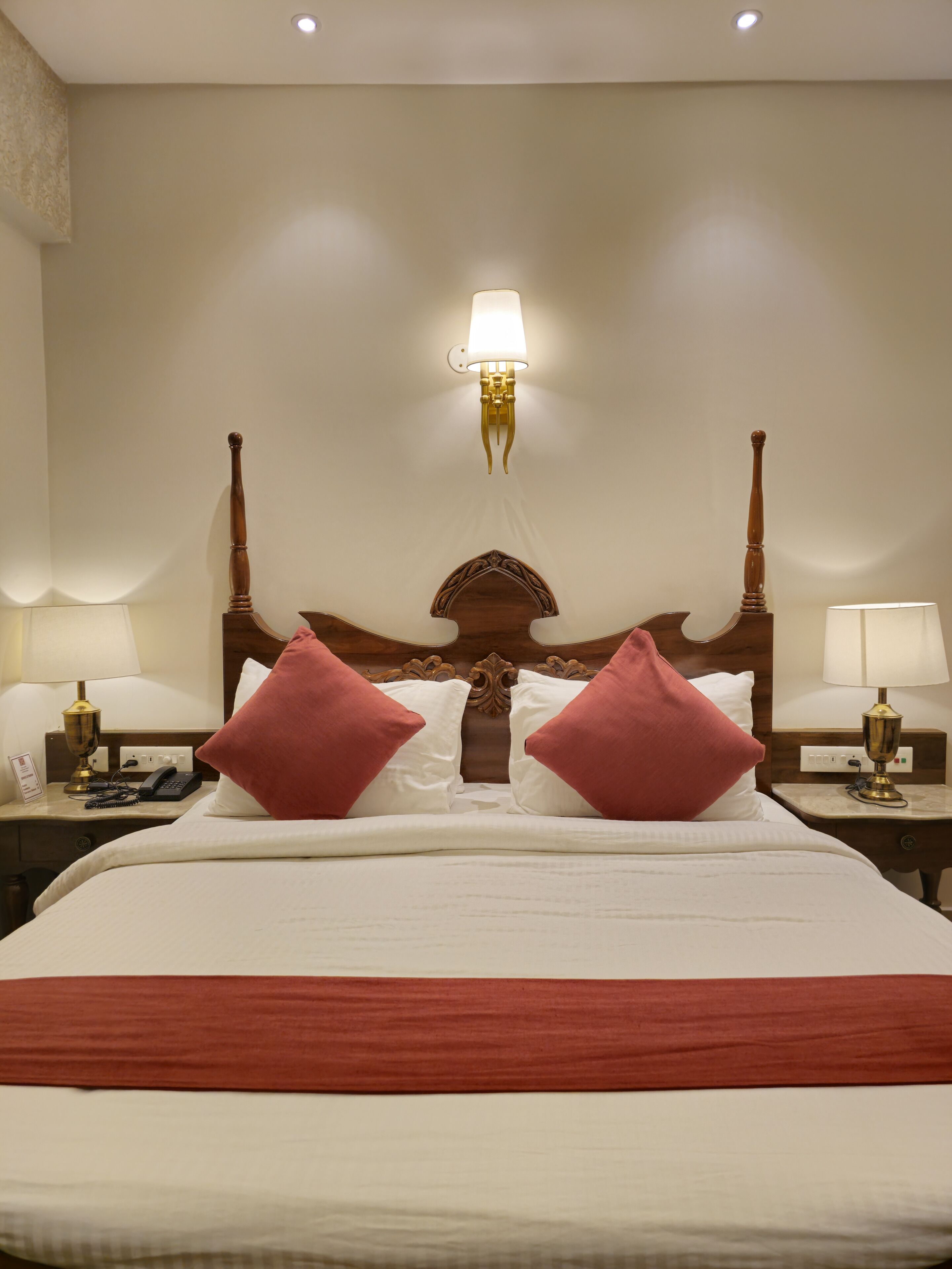 Habitación de hotel con una cama grande, dos mesitas de noche, una lámpara de pared y un cabecero decorativo.