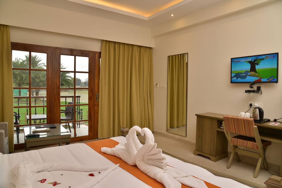 A hotel room with a bed, a desk, a chair, a television, and a view of a garden.