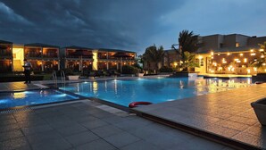 A swimming pool with a tiled deck, a building with multiple balconies, and a palm tree. - The creek boutique resort & spa (Bolpur)