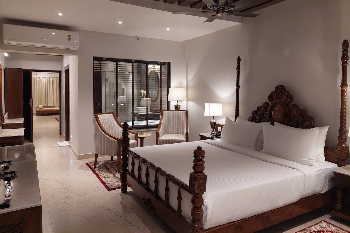 A hotel room with a four-poster bed, a sitting area with two chairs, a small table, and a ceiling fan.