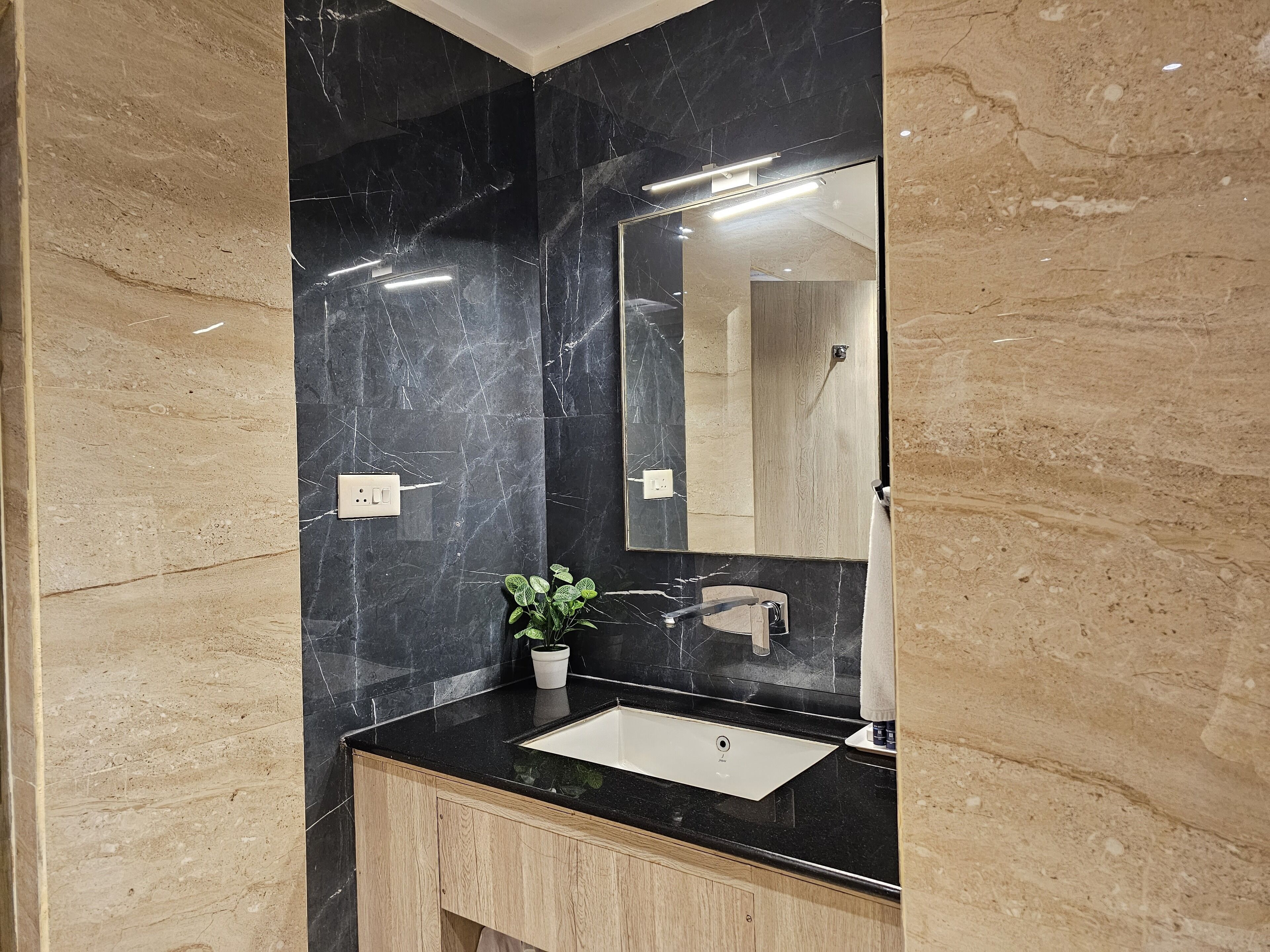 Un baño moderno con pared de mármol negro, lavabo blanco y mueble de madera.