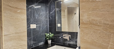 Un baño moderno con pared de mármol negro, lavabo blanco y mueble de madera.