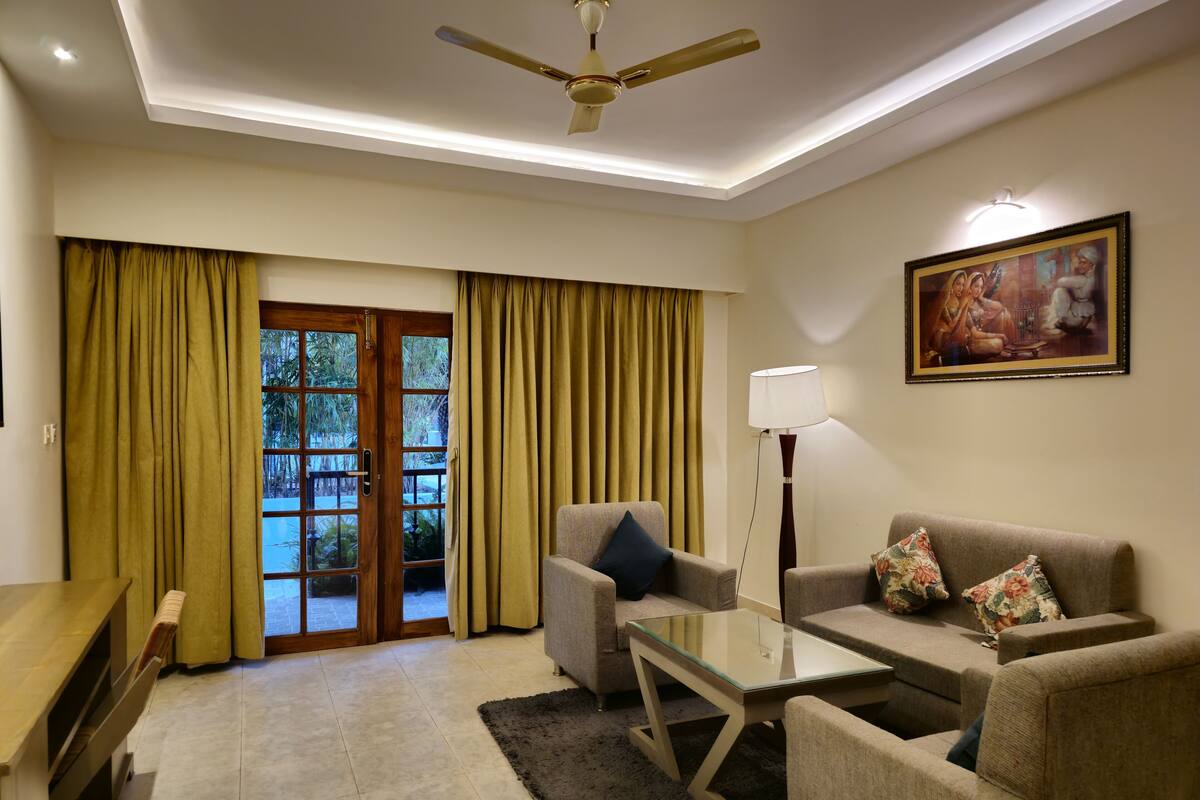 A living room with a glass-top coffee table, two sofas, a bench, and a ceiling fan.
