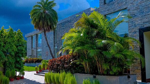 A modern building with a stone facade, surrounded by lush greenery and potted plants. - The creek boutique resort & spa (Bolpur)