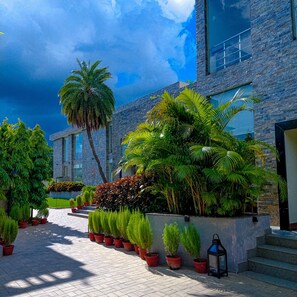 A modern building with a stone facade, surrounded by lush greenery and potted plants. - The creek boutique resort & spa (Bolpur)