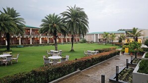 A hotel courtyard with outdoor seating, palm trees, and a brick building. - The creek boutique resort & spa (Bolpur)