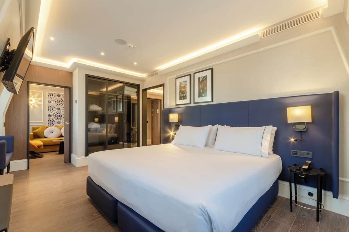 Una habitación de hotel moderna con una cama grande, lámparas de noche, un escritorio y un sofá.