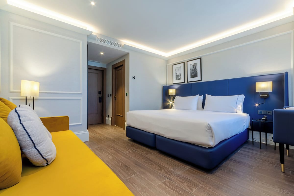 Una habitación de hotel con una cama grande, un sofá amarillo y un escritorio con una silla.