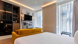 Ein Hotelzimmer mit einem großen Bett, einem gelben Sofa, einem Fernseher und einem Wandgemälde mit Stadtansicht.