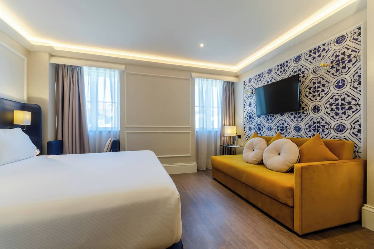 Una habitación de hotel con una cama grande, un sofá, un televisor de pantalla plana y papel tapiz estampado.