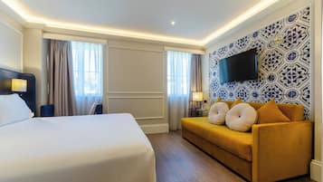 A hotel room with a large bed, a sofa, a flat-screen TV, and patterned wallpaper.