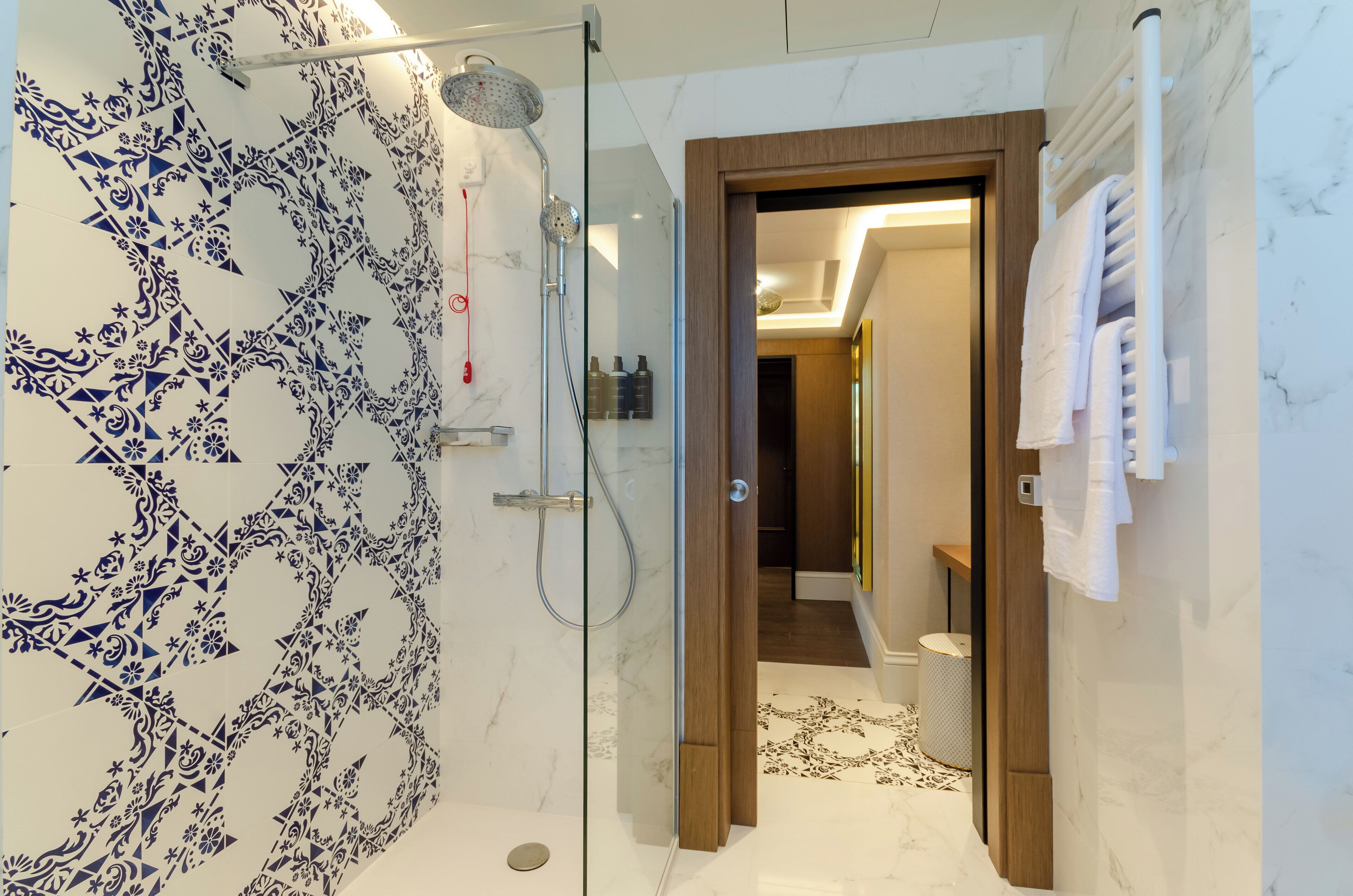 Un baño moderno con ducha cubierta por vidrio, paredes de mármol y una puerta de madera que da a otra habitación.
