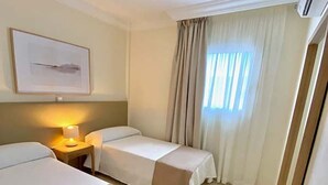 A hotel room with two beds, a bedside table with a lamp, a framed picture on the wall, and a window with curtains. - Luxury villa Masca with private heated pool (Costa Adeje)