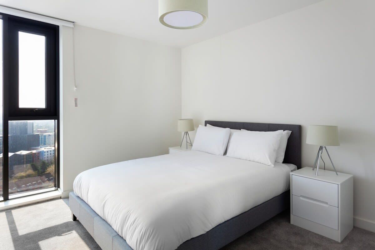 Une chambre moderne avec un grand lit, deux tables de chevet avec des lampes et une porte-fenêtre coulissante donnant sur un balcon.