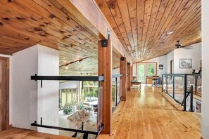 A spacious interior with wooden floors and ceiling beams, a balcony with a glass railing, and a view of an outdoor patio area. - Stunning European waterfront escape with hot tub (Lyndhurst)