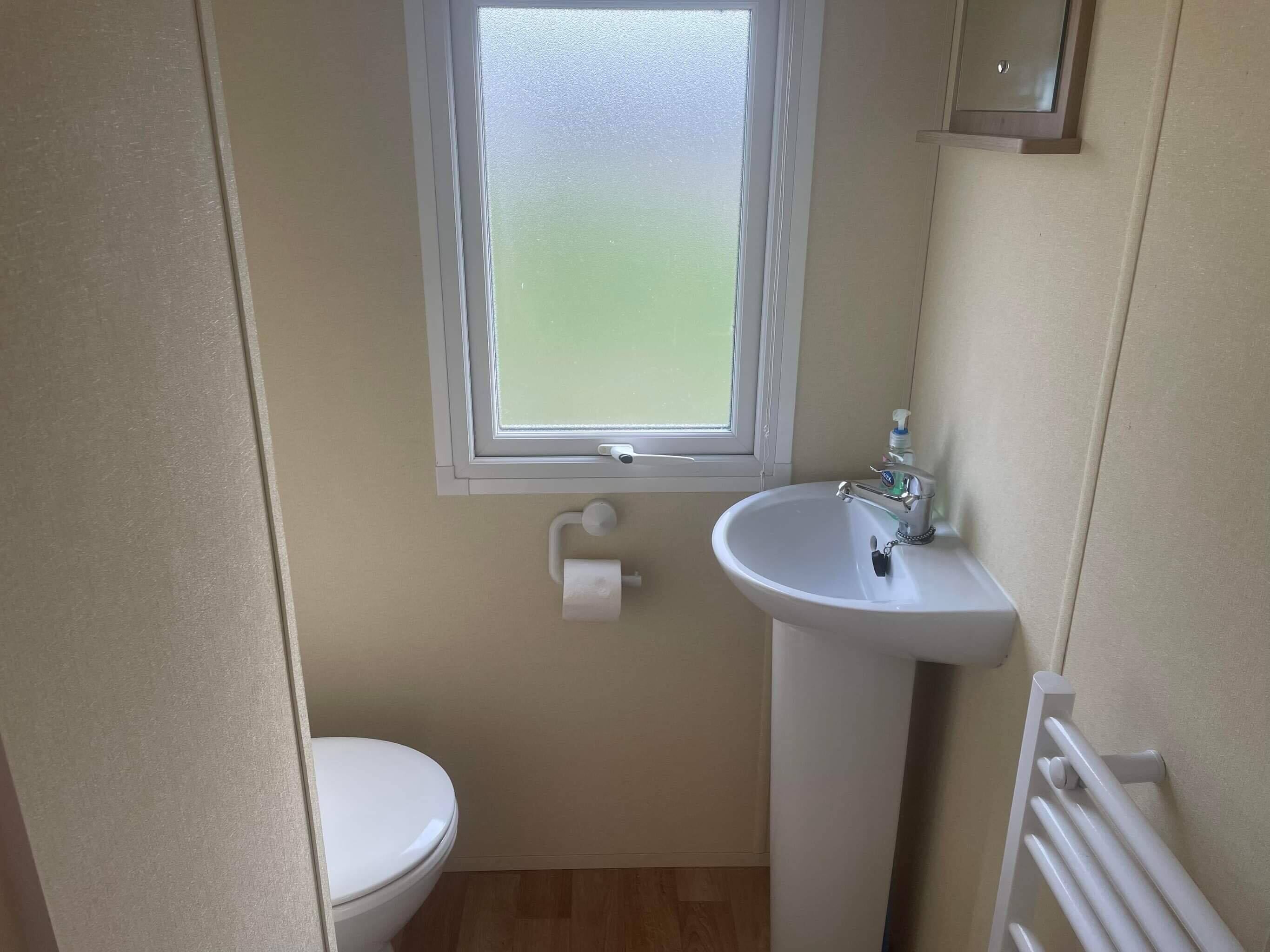 Un baño pequeño y limpio con inodoro, lavamanos y ventana.